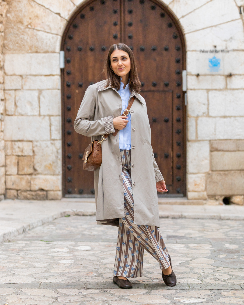 Gabardina Copenhagen color beige combinada con camisa, pantalón de rayas y bolso.