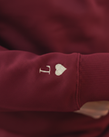 Primer plano del bordado de inicial y corazón granate en la manga de la sudadera granate