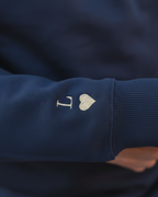 Primer plano del bordado de inicial y corazón en la manga de la sudadera azul marino