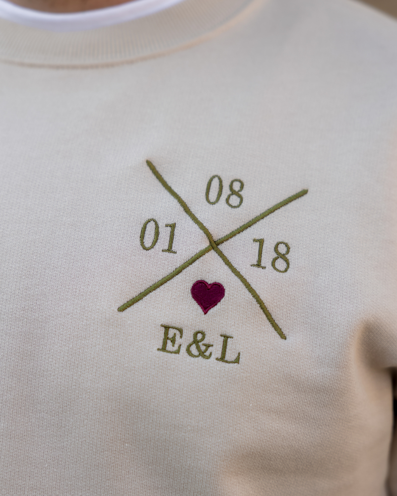 Primer plano del bordado de la X personalizada y corazón granate sobre la sudadera beige