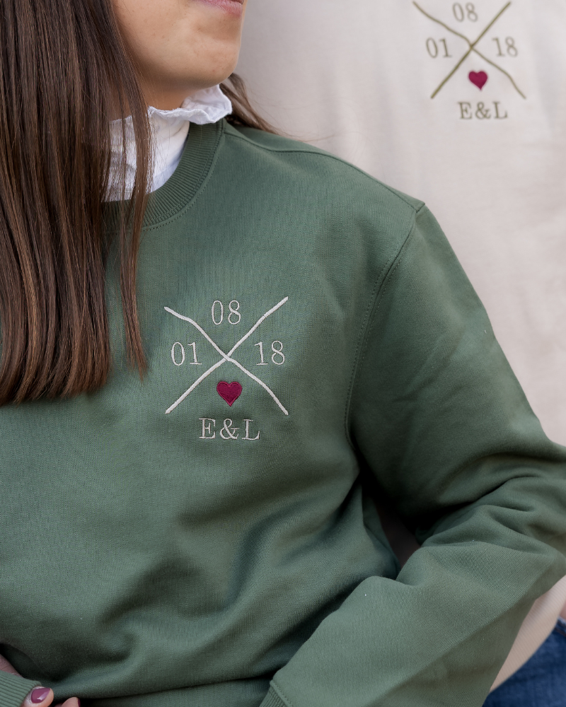 Primer plano del bordado personalizado X y corazón granate, mostrando textura y calidad sobre la sudadera verde caqui