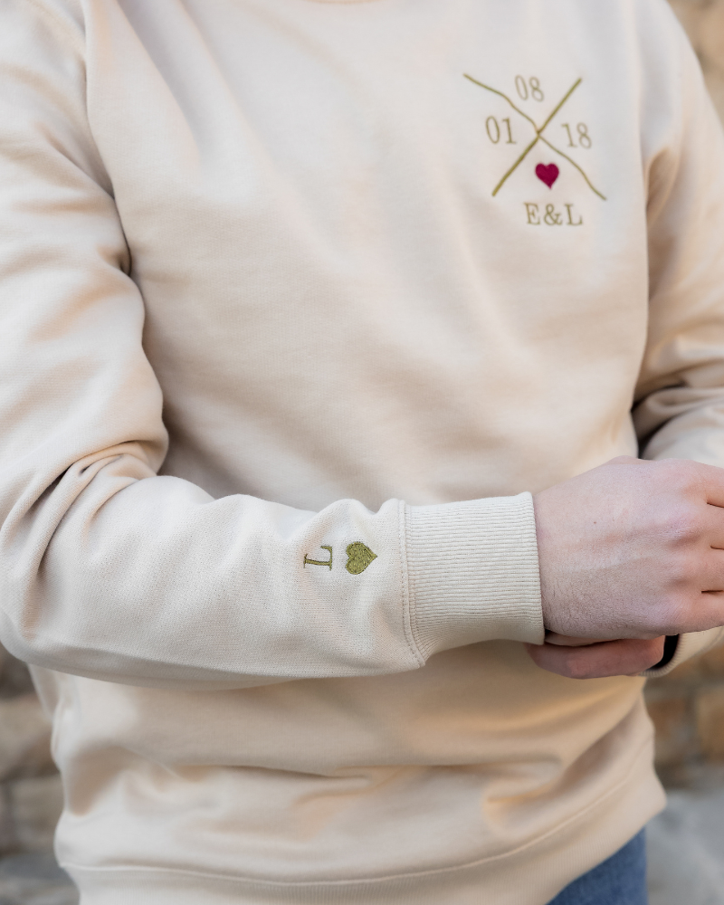 Modelo vistiendo sudadera beige unisex, vista lateral derecha, bordado de X persoanlizada y corazón granate visible y bordado inicial y corazón en la manga