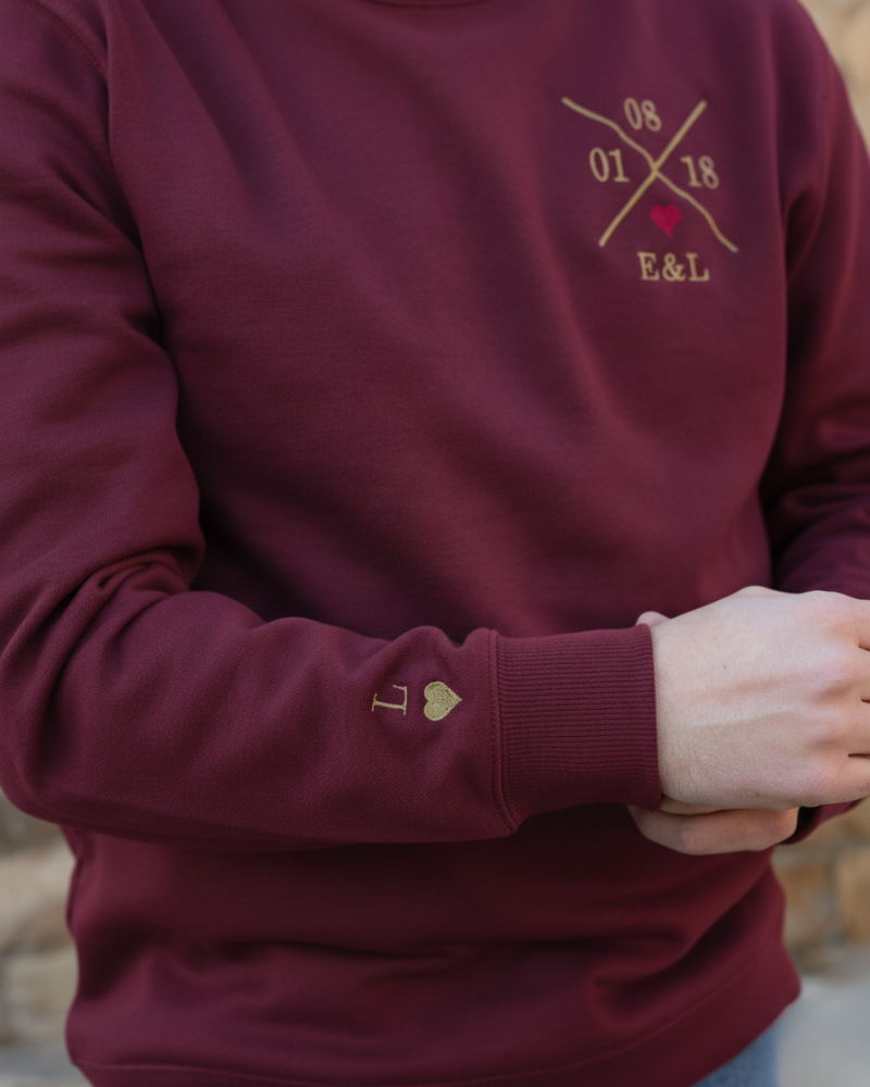 Modelo vistiendo sudadera granate unisex, vista lateral derecha, bordado personalizado y corazón granate visible en el pecho y bordado inicial y corazón manga